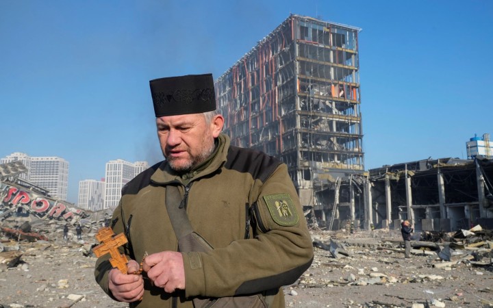 Fotovýber: Kňaz sa modlí na mieste zbombardovaného obchodného domu v Kyjeve. (AP